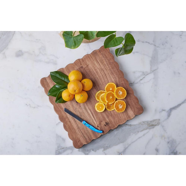 Scalloped wooden cutting board with oranges on a marble surface