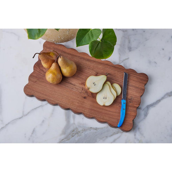 Scalloped wooden cutting board with pears and a knife on a marble surface