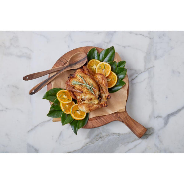 Roasted chicken with oranges and sage on a wooden board on a marble surface