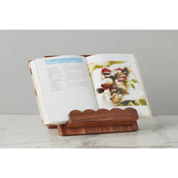 Wooden book stand holding an open cookbook on a white surface with a gray background