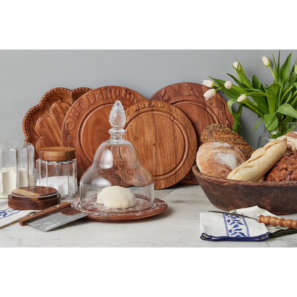 Wooden bread boards and a glass cloche on a table with bread and flowers.