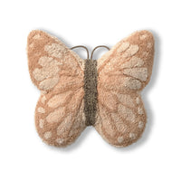 A plush butterfly-shaped decorative pillow in shades of beige and light brown with a textured, fuzzy surface, shown on a clean white background.