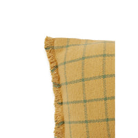 A close-up of a woven throw pillow or cushion corner in a mustard yellow fabric with a green plaid pattern and fringed edge, shown on a plain white background.