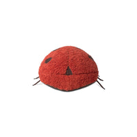 A red fuzzy ladybug-shaped plush toy or cushion with black embroidered eyes and legs, photographed on a plain white background.