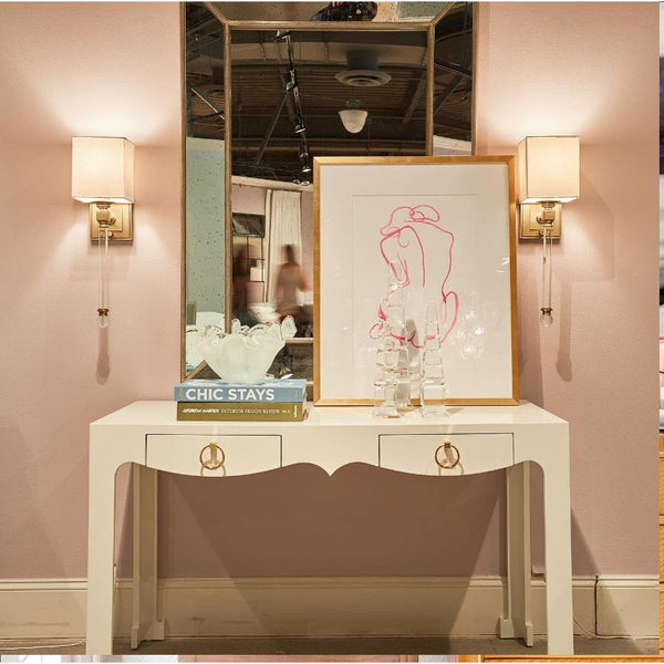 Elegant entryway with a white console table, the Lithograph Bold Contour I Framed Art by Shadow Catchers Art, and books, featuring a pop of color from vibrant wall sconces reflecting in a large mirror.
