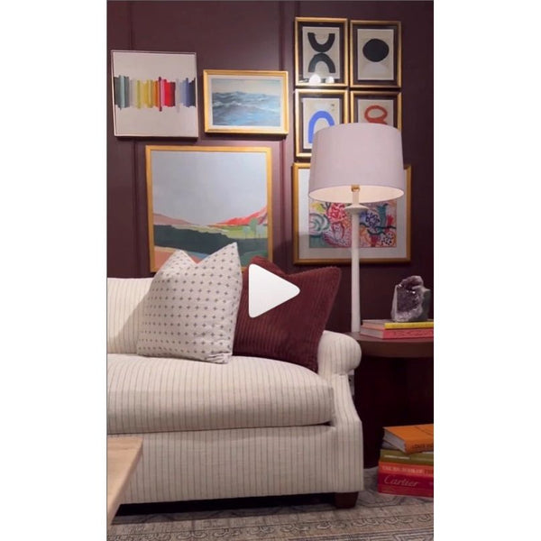 A cozy living room featuring a striped sofa, accented with pillows and enriched by Definition VIII Blue Modern Framed Art by Shadow Catchers Art on the walls. A side table and a floor lamp introduce a contemporary touch to the space.