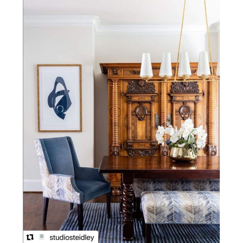 Elegant dining room featuring a wooden cabinet, the Gizmo in Navy II Gold Wood Frame Wall Art by Shadow Catchers Art, a blue chair, and a flower centerpiece on the table.