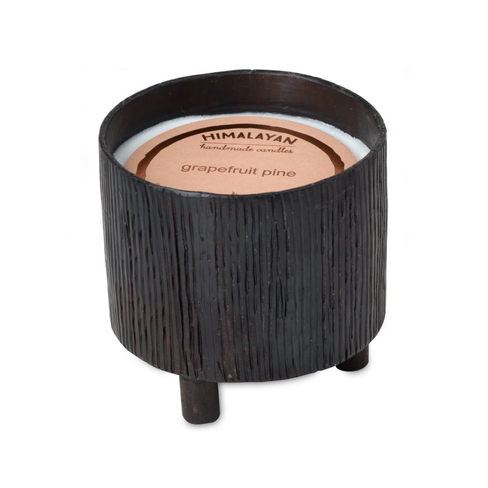 A Blacksmith Forged candle by Himalayan Trading Post, with a "grapefruit pine" scent in a black textured vessel on three legs.