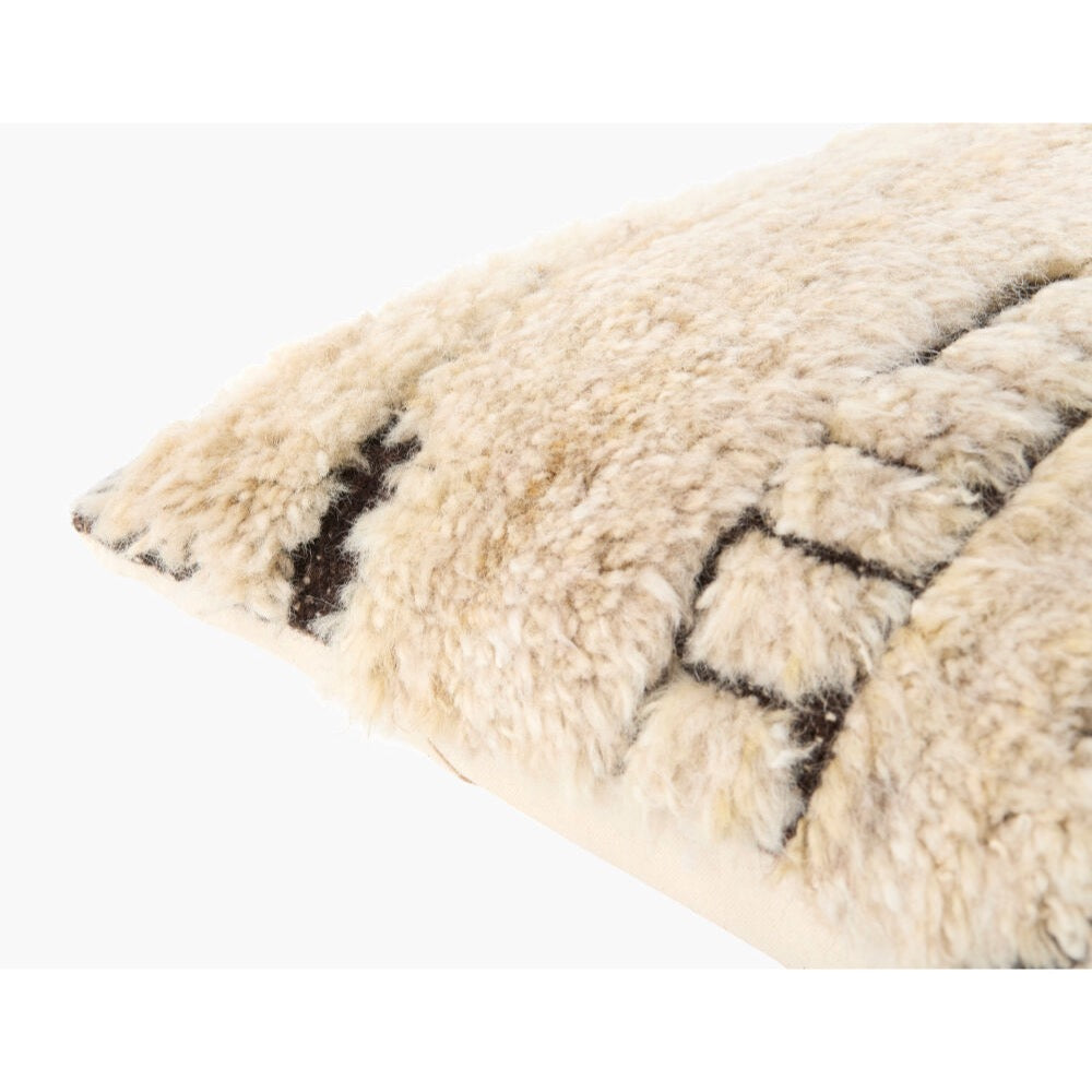 Close-up of a fluffy sheepskin or wool throw pillow in cream with dark brown geometric woven patterns, shown on a plain white background.