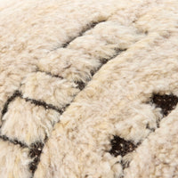 Close-up of a textured wool or sheepskin-like surface in warm cream/beige with dark brown stitched or shadowed geometric lines.
