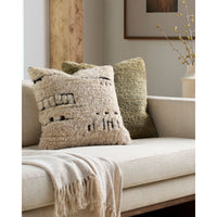 Two textured throw pillows on a light beige sofa in a styled living room setting. The front pillow is cream with black geometric woven patterns, and the back pillow is olive green.