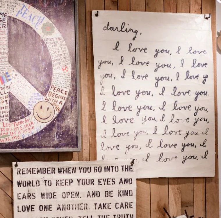 Handwritten message on a fabric poster with a peace symbol and smiley face, against a wooden wall.