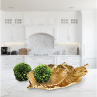 Alegra Leaf Trays by Napa Home & Garden hold two green balls on a marble counter with white cabinets in the background.