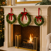 Three Napa Home & Garden Hanging Boxwood Wreaths (set of 3) with red bows hang above a lit fire, near a Christmas tree.