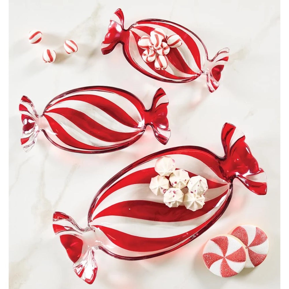 Three red and white striped candy-shaped glass bowls arranged on a light marble surface, with small red-and-white peppermint candies placed around them.