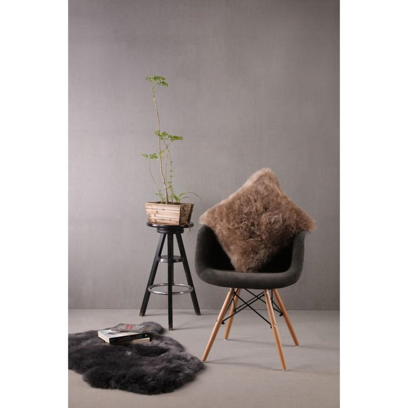 Modern chair with an Auskin Longwool Sheepskin Pillow, a plant on a stool, a fur rug, and books against a gray wall setup.