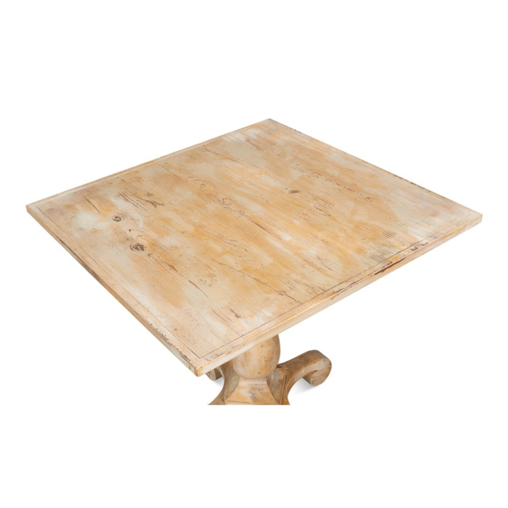 A square wooden table with a distressed light beige finish and a carved pedestal base, shown on a plain white background.