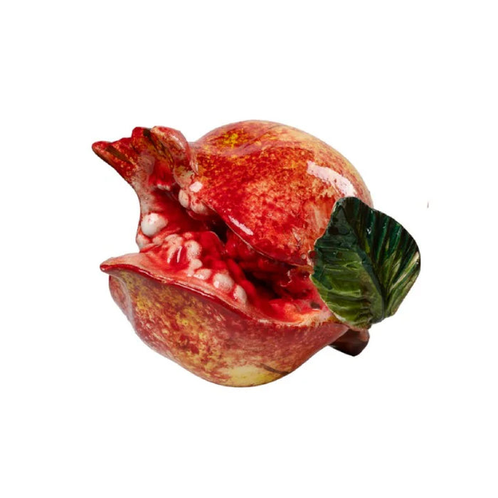 a ceramic figurine of a pomegranate that is open with a green leaf