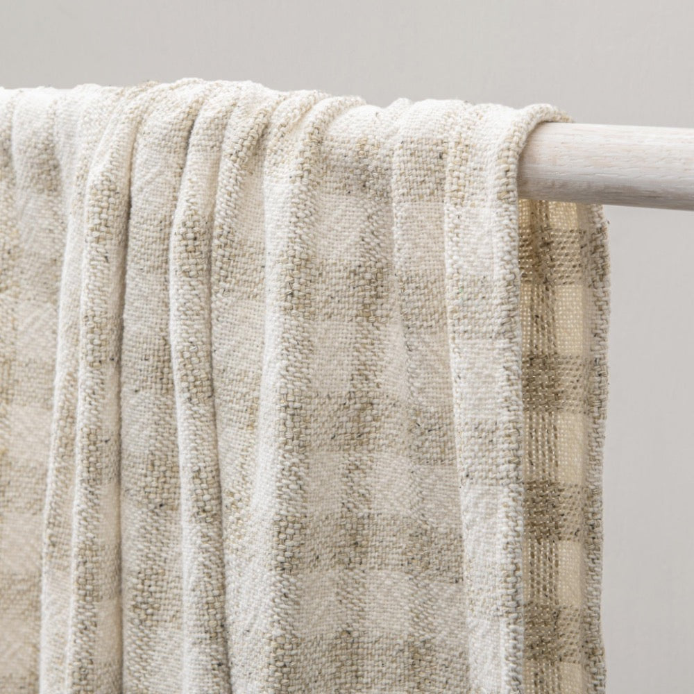 Textured beige blanket draped over a white rod against a neutral background
