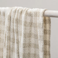 Textured beige blanket draped over a white rod against a neutral background