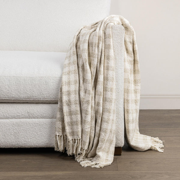 Beige plaid blanket draped over a gray sofa against a neutral wall.