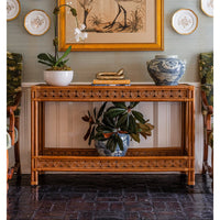 Decorative console table with vases and plants in a room with a painting and plates on the wall.