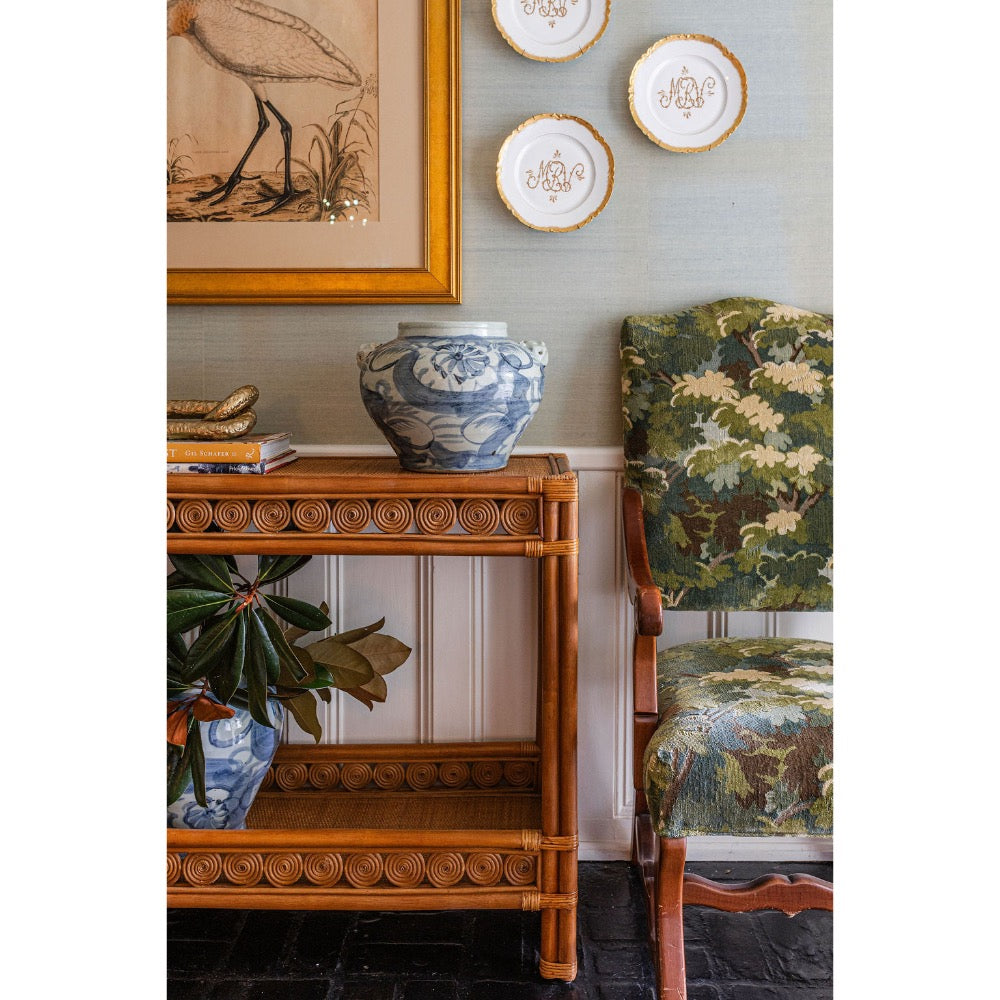 Decorative interior setting with a wicker console  table, blue and white vase, and patterned chair.