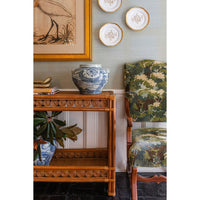 Decorative interior setting with a wicker console  table, blue and white vase, and patterned chair.