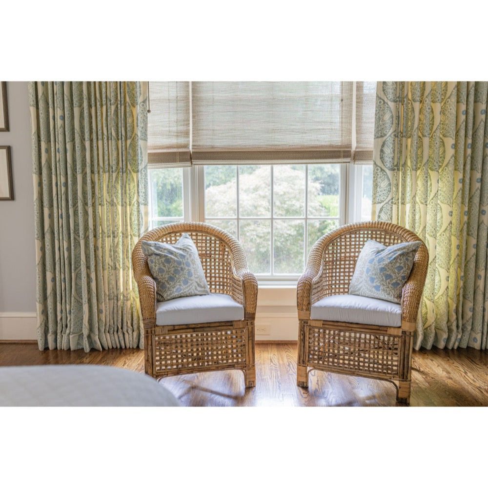 Two wicker chairs with cushions in a room with large windows and decorative curtains.