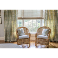 Two wicker chairs with cushions in a room with large windows and decorative curtains.