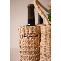 A close-up of a woven natural-fiber wine bottle carrier holding dark wine bottles, with part of a matching carrier visible at the right edge against a soft beige background.