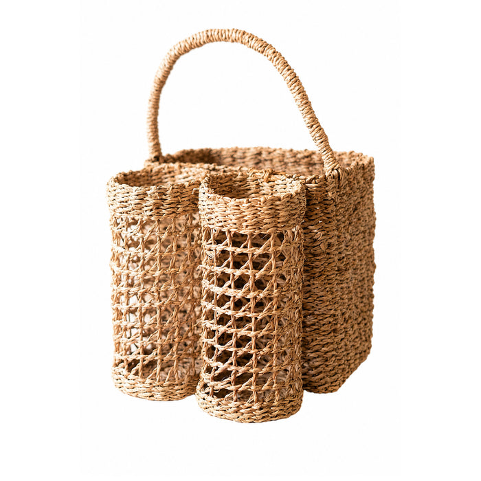 A natural woven straw basket with a single curved handle, featuring two cylindrical compartments with open lattice weave on the front, shown on a plain white background.