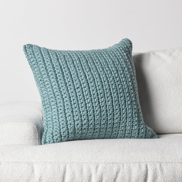 The Classic Home Outdoor Performance Prism Pool Blue Pillow rests on a white sofa against a plain background.