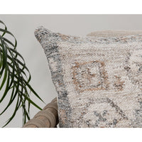 The Classic Home Outdoor Performance Lukens Pillow sits on a beige chair next to a leafy plant against a light background.