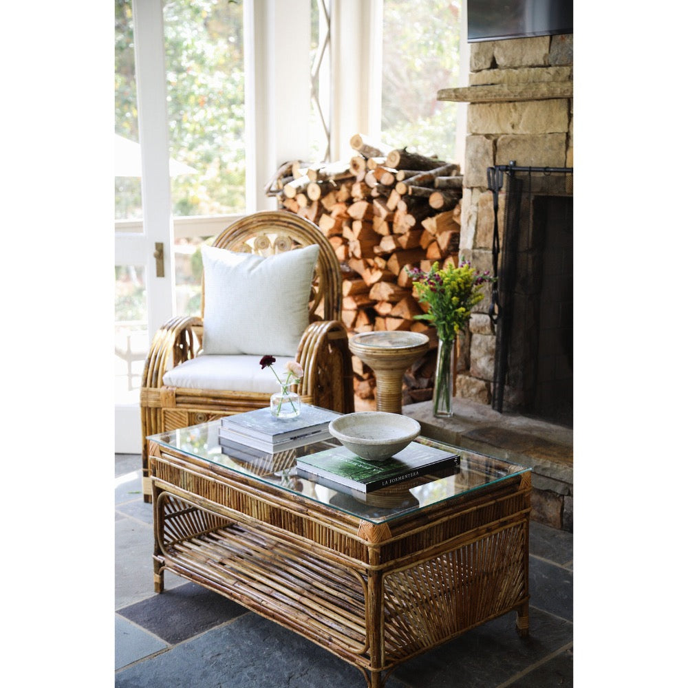 Rattan chair and coffee table with a fireplace and stacked wood in the background