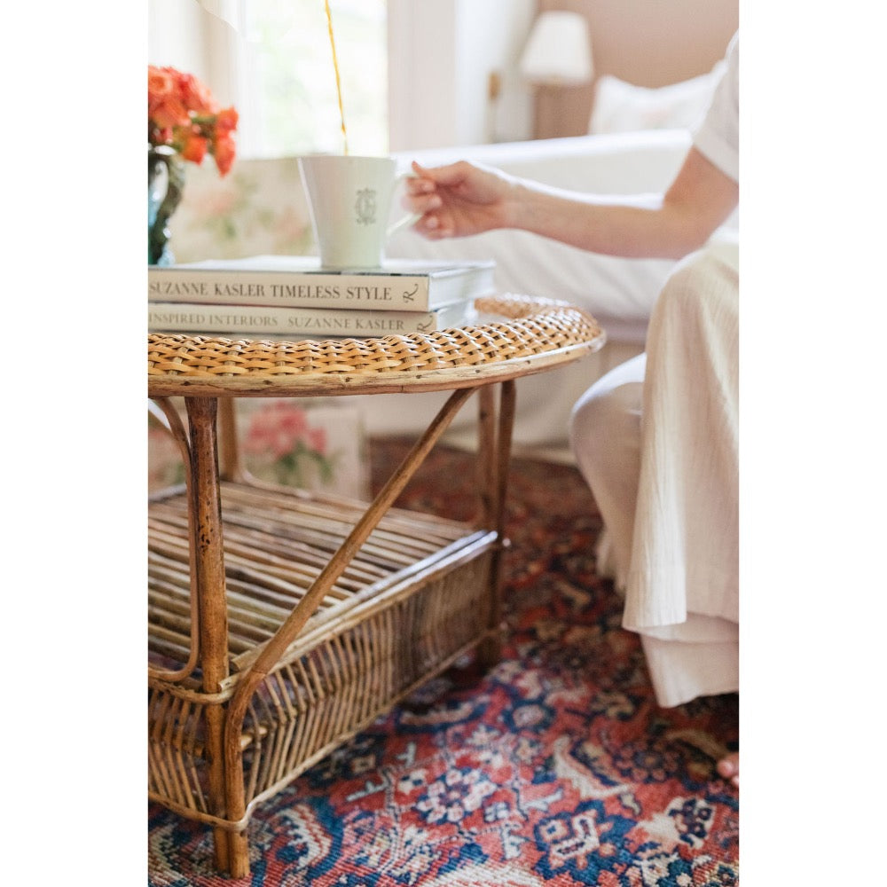 Wicker side table with books on a patterned rug, blurred background