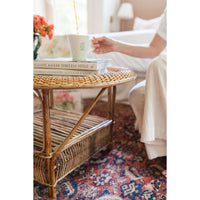 Wicker side table with books on a patterned rug, blurred background