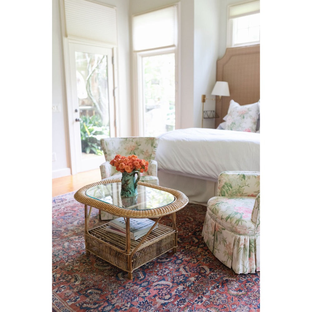 Living room with floral armchair, glass coffee table, and bed in the background