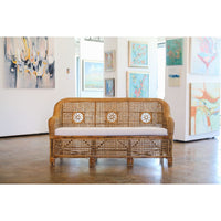 Wicker sofa with white cushion in a room with abstract paintings on the wall.