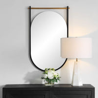 Round mirror with black frame on a white wall above a dark wooden cabinet with a lamp and floral arrangement.