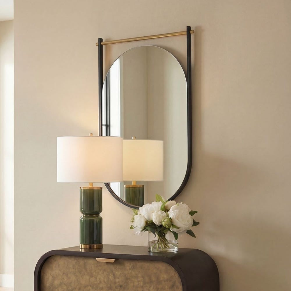 Decorative mirror with a lamp and flowers on a console table against a beige wall.