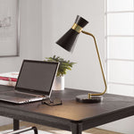 The Uttermost Black + Gold Desk Lamp with a black marble base sits on a modern dark wood desk beside a laptop.