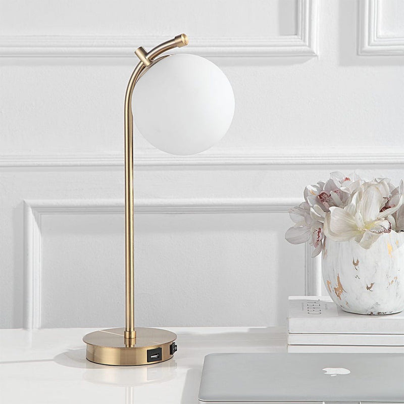 The Uttermost Glass Globe Desk Lamp is shown beside a laptop and flower vase on a sleek white desk.