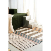 A striped area rug in beige, brown, and blue tones with a textured woven pattern, styled in a modern living room setting next to a dark green sofa and a small white side table.