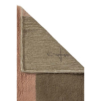 A close-up of a folded area rug showing its striped jute backing and a solid brown textured section, with a dusty pink border visible on the left side against a white background.