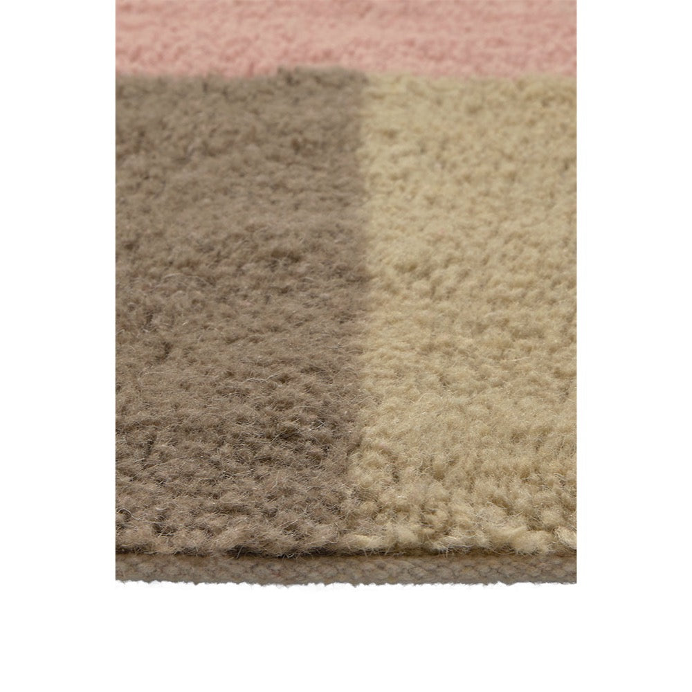 Close-up of a shaggy area rug showing a color-blocked pattern with a dusty pink section at the top, a taupe-brown section on the left, and a warm beige section on the right.