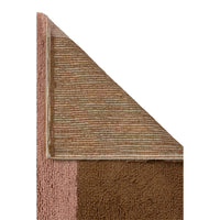 Close-up of underneath a rug corner showing two color blocks: a warm pink and brown section against a white background.