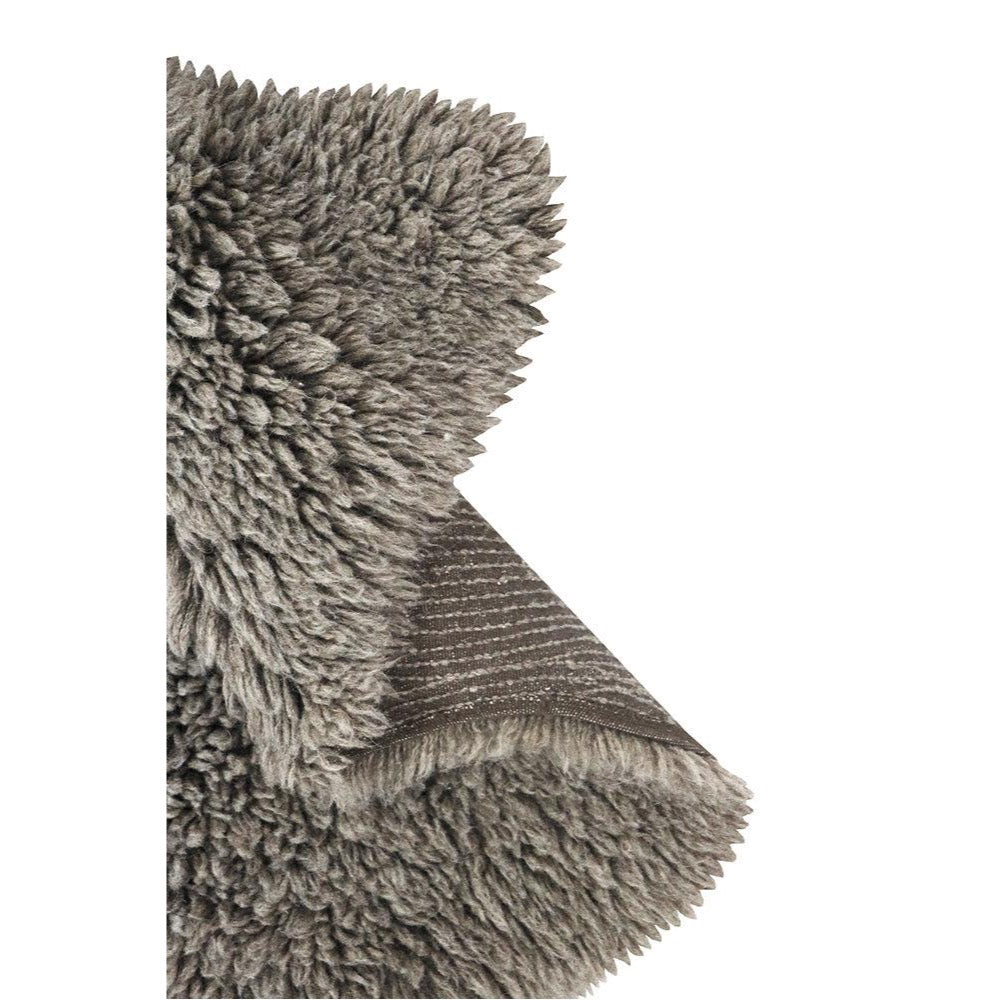 Close-up of a gray shaggy rug with a folded corner showing the textured underside and fringe edge, photographed on a white background.