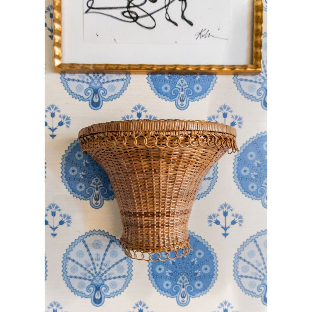 Wicker wall shelf against a decorative wallpaper with blue and white patterns
