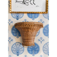 Wicker wall shelf against a decorative wallpaper with blue and white patterns